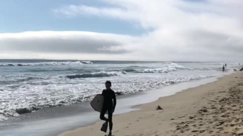 Boogie boarder walks down beach with flipper feet