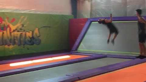 Guy multiple back flips on orange and purple trampoline