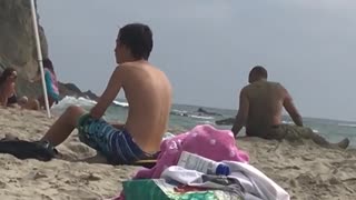 Old shirtless man puts stick in ear at beach plays with sand