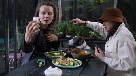 Two girls trying to take a selfie with cute brown and white dog over while having lunch