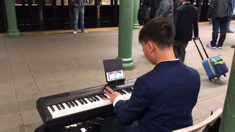 Man in blue suit plays piano in subway station