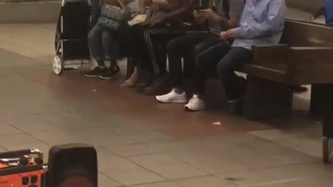 Guy red shirt black hat dancing sits between people subway bench