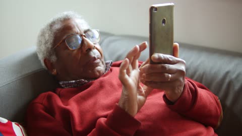 An Elderly Man Using a Cellphone on a Couch