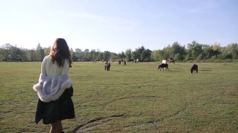 Beautiful hipster mixed race girl walking with herd of horses in countryside