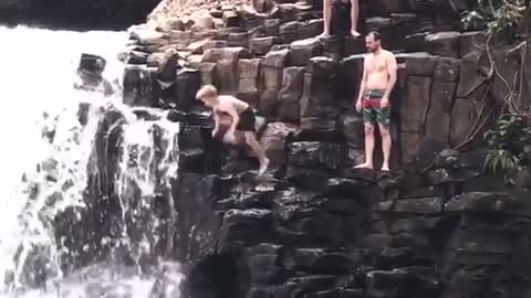 Boy in black water shorts jumps off cliff bellyflop