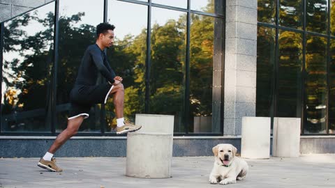 Young man stretching after his training in city center with his white labrador dog beside him in