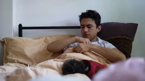 Hispanic man in bed waking up sick with emotional support dogs and blowing nose