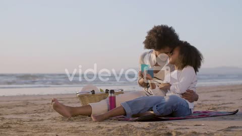 Loving Mother And Daughter Drinking Tea And Talking While Sitting On A Blanket And Having A Picnic O