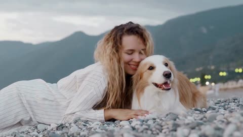 Pretty woman relaxing at the beach with her dog at sunset on the background of mountain