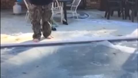 Fat guy black shirt camo pants jumps into frozen pool with blue pool noodle