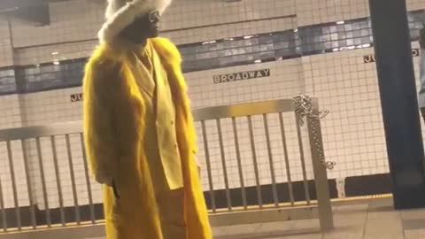 Man wearing big yellow fluffy coat and suit at subway station