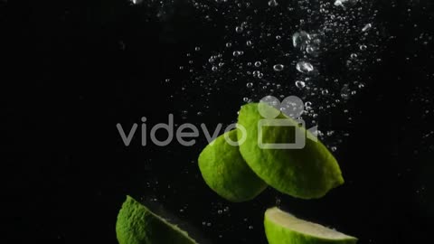 Lime citrus fruit isolated, pieces of split and cut green lime dropping into water on a black backgr