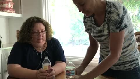 Lady tries to squeeze water bottle into face of other lady hits herself magic trick