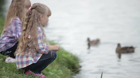 Two cute girls at park feeding ducks and smiling at camera