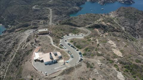 drone view of serpentine winding mountain road to lighthouse on top of rock against background of