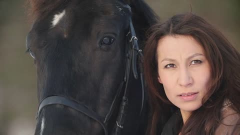 Beautiful rider young woman and her black horse posing in snowy forest