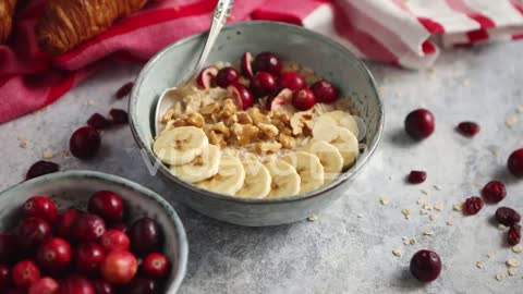 Ceramic bowl of oatmeal porridge with banana fresh cranberries and walnuts