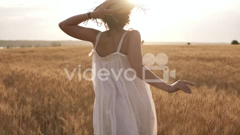 Young Woman Running In The Wheat Field While Holding Her Straw Hat
