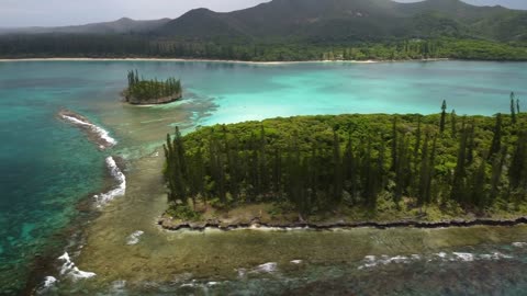 An aerial tracking shot passes a small island near the Isle of Pines