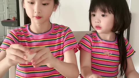 Two little girls are breaking eggs by touching them with their foreheads.