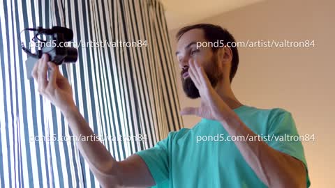 A young blogger records a video with himself on his camera in his room near window