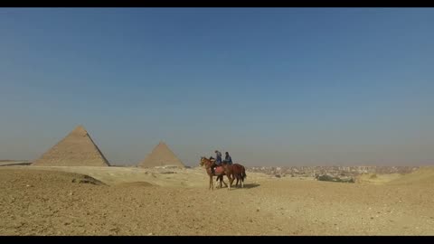 Woman riding horse with local man in front of Giza pyramids, Egypt