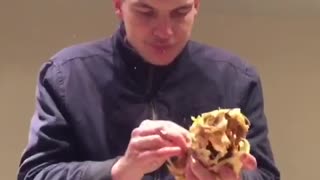 Guy in blue jacket eats large piece of chicken