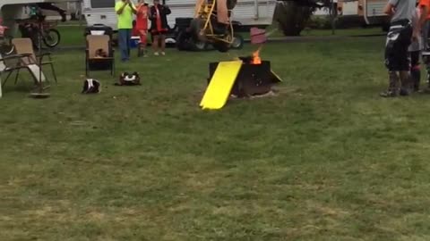 Guy in orange shirt does ramp jump over small fire on mini motorcycle