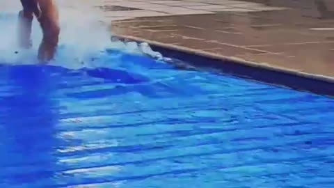 Guy in red shorts running on top of blue sheet in pool