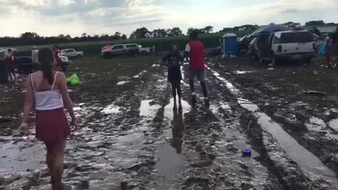 Music black guy wearing red shirt pushes girl wearing black into mud
