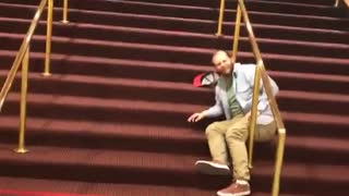 Blue shirt tries slide down gold railing on red stairs and falls