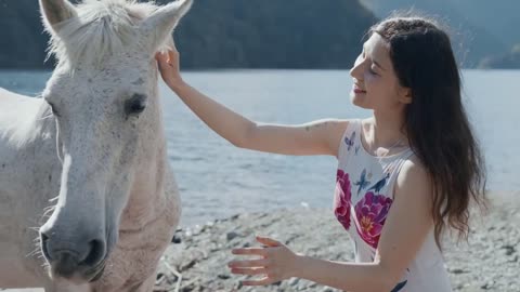 Pregnant woman petting white horse by the mountain lake at beautiful sunlight