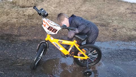 little boy playing with bike in puddle