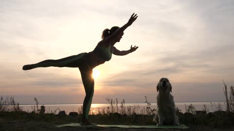 Woman and her dog doing yoga in front of the sea