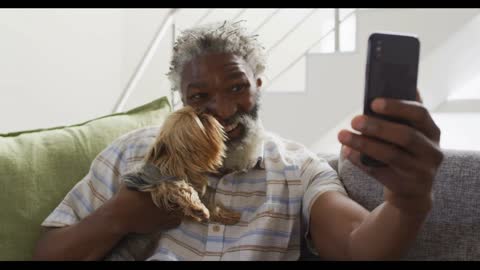 Senior man holding his dog having a video chat on smartphone at home