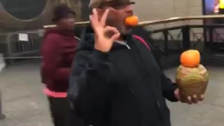 Guy balancing fruit with ok sign standing still subway