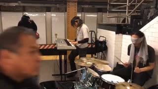 The drummer blindfolded is playing drums with rock music on the subway street