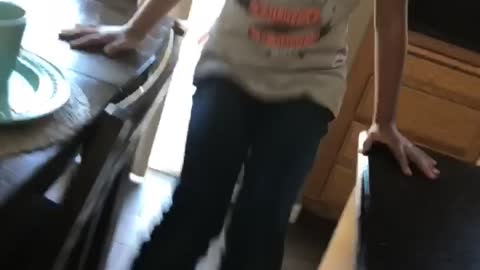 Girl balancing swinging between counter and chair falls backwards on floor