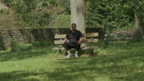 A mixed race black man sitting on a bench, playing and throwing the ball
