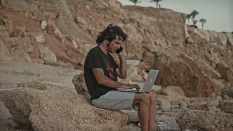 Man Sitting on a Rock While Using His Laptop and Smartphone