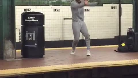 A woman in grey sweatsuit dances on subway station