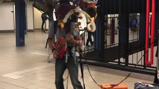 Man sings rudolph the rednose reindeer, plays guitar, other instruments on his back
