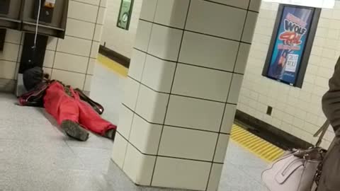 Guy in red laying next to payphone on subway platform