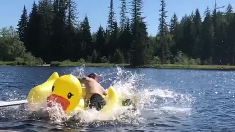 Man jumps on yellow duck inflatable toy in lake