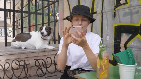 Girl in a bucket hat using her smartphone while waiting in a cafe with pretty dog