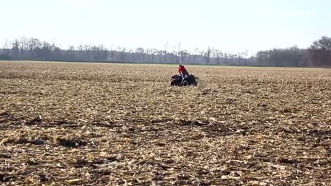 A kid in red rides a four wheeler on an open field and flips forward