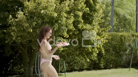 Cute Woman In Bikini Carrying Plate With Fruits To Friends Next To The Pool