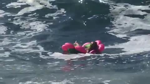 Woman in pink flower floatie crashes with waves
