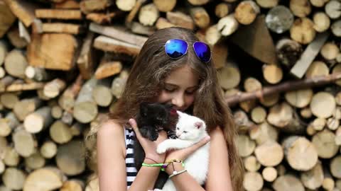 Beautiful girl in blue sunglasses holds in hands white and black cats