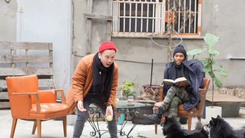 Medium shot of queer interracial couple tosses a ball with dogs in their urban garden
